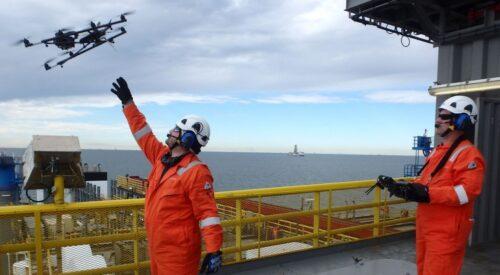 worker dressed in orange with arm outstretched toward drone