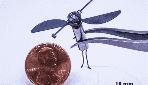 Tiny flying bot suspended by tweezers next to penny.